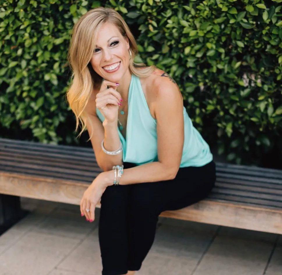 A woman sitting on top of a bench in front of bushes.