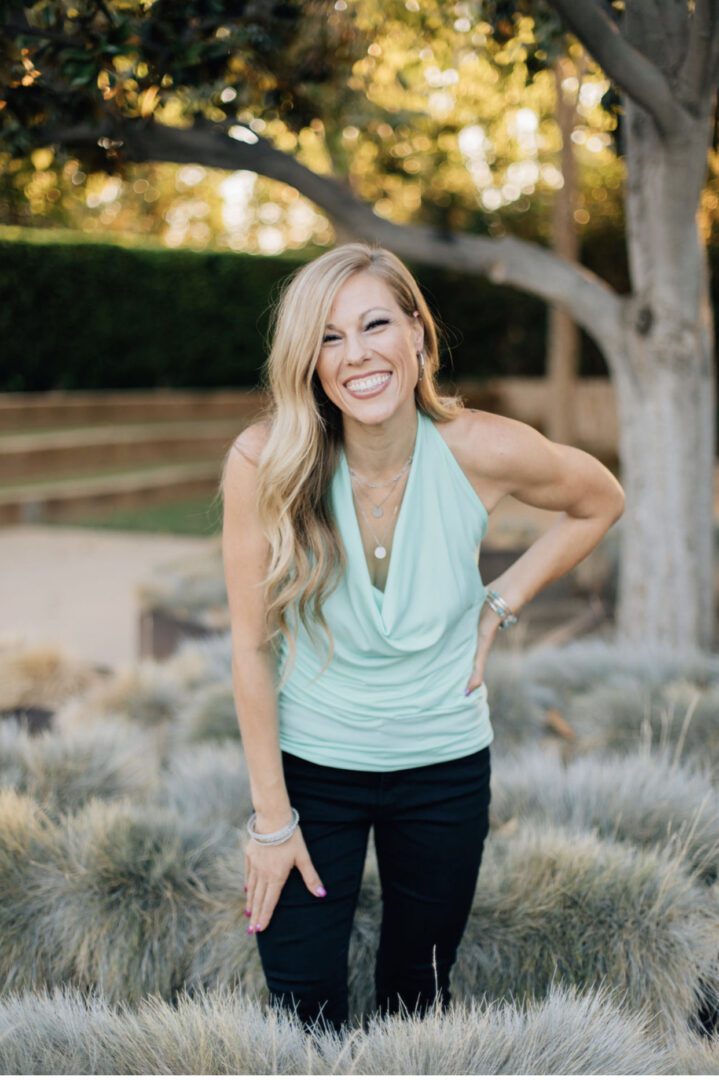 A woman standing in the grass wearing black pants and a blue top.